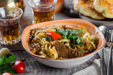 Traditional asian uzbek noodle lagman with vegetables and meat on rustic wooden table background....