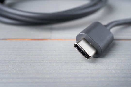 USB Type C connector with a grey cable on a wooden background. Shallow depth of field. Copy space in the bottom left corner.