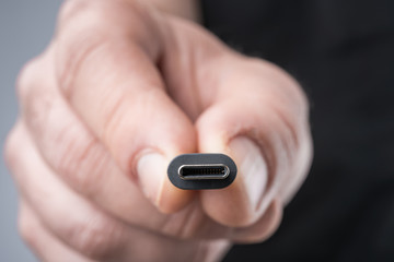 USB Type C connector with a grey cable being held in hand. Shallow depth of field.