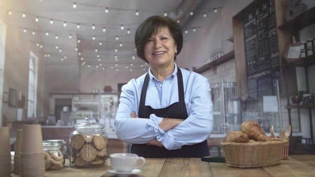 Portrait of happy beautiful confident cafe owner in a coffee house looking at camera and smiling. Pretty mature woman business owner with apron ans arm crossed. Businesswoman.