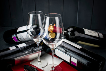 Two glass glasses with red wine bottles lying down and gray wooden background with red details