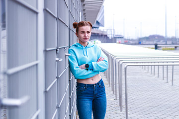 Girl in a blue crop top. Stylish streetwear for teens. Shooting near the gray grid. Blue jeans.