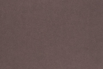 Brown colored paper. Texture of surface, fibers and irregularities are visible. View from above. Dark background or wallpaper