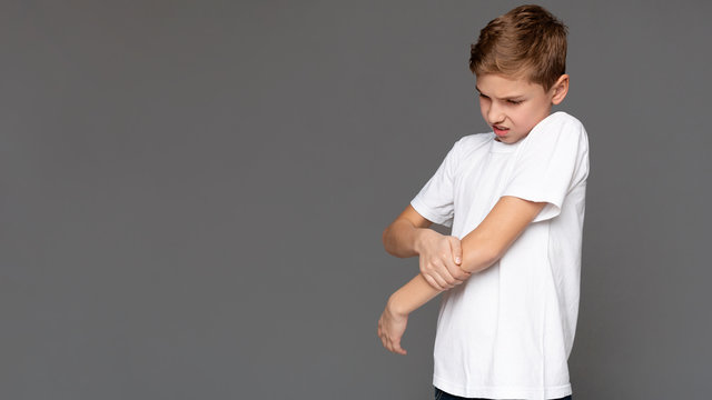 Sad teen boy holding his hurt hand, grey panorama background