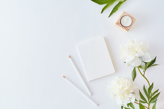 Flat lay blogger or freelancer workspace with a notebook and white peonies on a white table