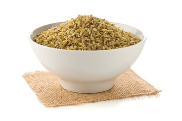 Heap of uncooked, raw freekeh or firik, roasted wheat grain, in white bowl over white