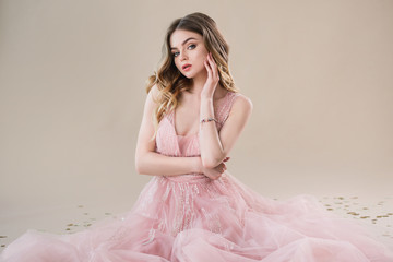 attractive young woman portrait in tender pink lace dress sits on beige background in studio