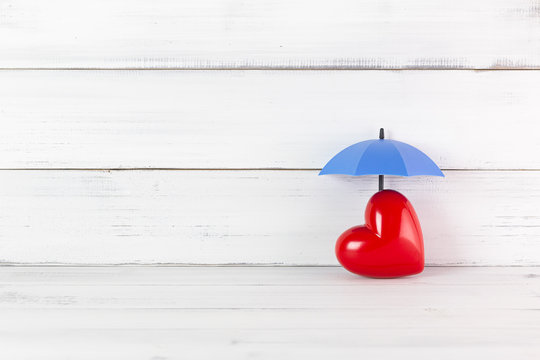 Red Heart under Umbrella on white wood background. Proect love or Heart Concept with Copy Space.