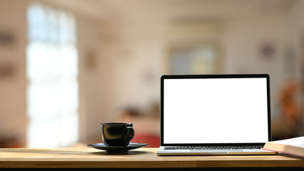 Photo of white blank screen laptop, black coffee cup and coasters on the wooden working desk over blurred modern cafe background. - obrazy, fototapety, plakaty