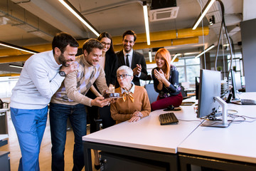 Young colleagues celebrate an senior colleague's birthday at the office and bring a cake