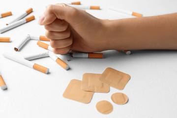 Nicotine patches and woman breaking cigarettes at white table, closeup