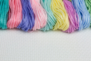 row of pastel colored skeins of embroidery threads on white cotton canvas