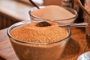 Additives to hot drinks.  Cane sugar, white sugar and honey with a special wooden spoon with selective focus on blurred background. Unhealthy carbohydrates. Brown and white sugar, organic honey