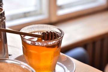 Additives to hot drinks.  Glass with honey with a special wooden spoon and selective focus on blurred background. Healthy carbohydrates. organic honey