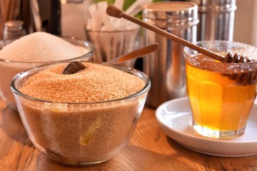 Additives to hot drinks.  Cane sugar, white sugar and honey with a special wooden spoon with selective focus on blurred background. Unhealthy carbohydrates. Brown and white sugar, organic honey