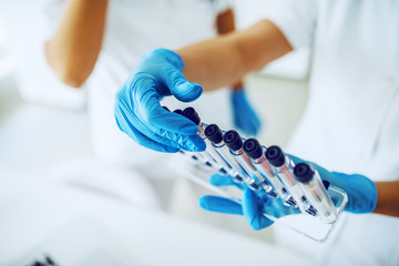 Close up of lab assistant with sterile rubber gloves holding stand with test tubes with blood...