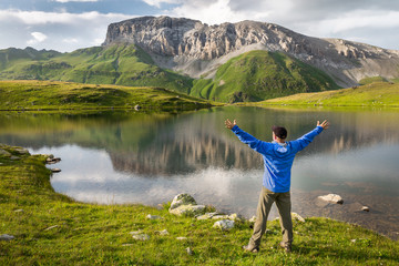 Male hiker near lake with arms stretched out to enjoy the rocky mountain