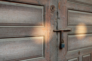 Closeup of rusted metal aged latch and padlock over weathered wooden door