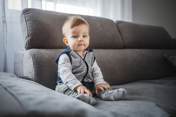 Fototapeta premium Cute little boy sitting on couch in living room and looking at camera.
