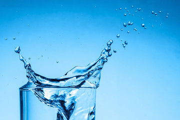 Fototapeta na wymiar Water splash in a glass cup on a blue background