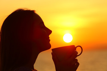 Lady holding coffee mug at sunset on the beach