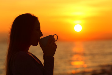 Woman drinking coffee at sunrise on the beach