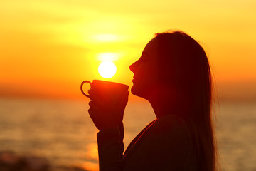 Woman drinks coffee at sunrise on the beach