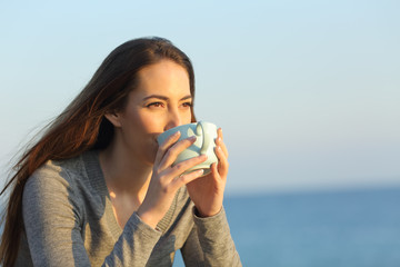 Woman drinking coffee on the beach at sunset