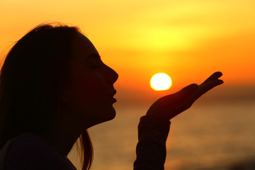 Profile of a woman blowing or kissing sun at sunset