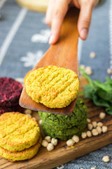 Vegan chickpea burgers cutlets or patties. Healthy vegan diet food. Woman hands holds mixed vegetables yellow pumpkin, orange carrot, green spinach and red beet bean cutlets with wooden spatula