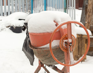 Dirty concrete mixer forgotten on the construction site under the snow.