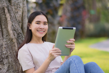 Beauty women using tablet reading E-book sitting in city park morning fresh