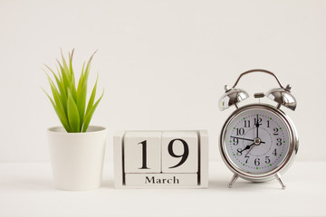 March 19 on a wooden calendar next to an alarm clock and a flower on a white background. The concept of one day a year.Significant date or event