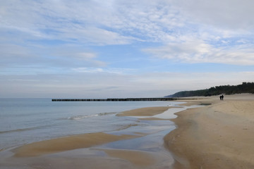 A beach with breakwaters in Dziwnowek / Poland on the Baltic Sea in the fall after the season. Empty and only two walkers.