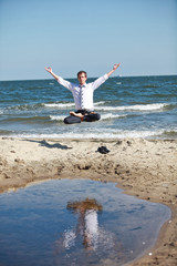 Perfection - caucasian man in lotos pose, with his arms raised,levitates above the beach