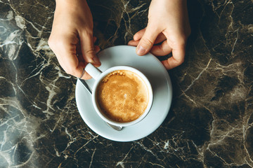 Top view girl holding a cup of delicious aromatic coffee on a marble table
