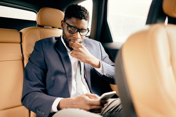 Businessman in a suit sits in a car back seat using his phone.