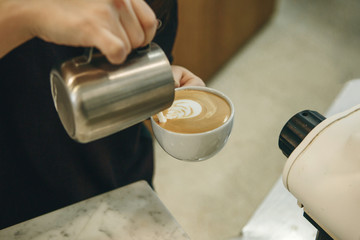 Barista makes delicious and aromatic coffee and draws a drawing on the foam