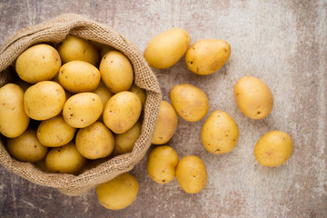 Sack of fresh raw potatoes on wooden background, top view.