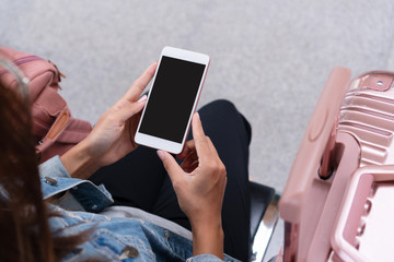 Young traveller girl in jeans jacket with smart phone, pink bag and luggage waiting for the train on the platform, copy space, travel or transportation concept