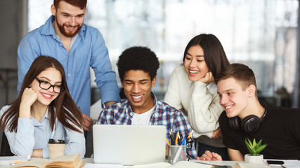 Happy college classmates using laptop in library