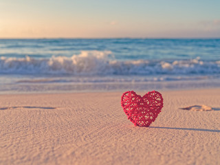 Tropical background for St. Valentine's Day. A red wicker heart is located on a sandy beach. Behind is the sea or ocean. Love of travel. - Powered by Adobe