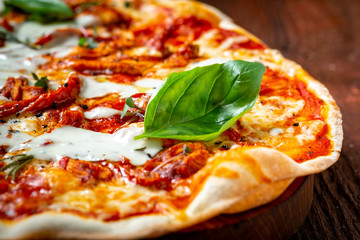 Lange Pizza Margarita mit sonnengetrockneten Tomaten und Basilikum auf einem Holzbrett, Nahaufnahme. Italienische Küche im rustikalen Stil