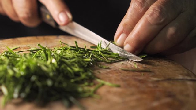 Old lady cutting kaffir lime leaves on a wooden board. Prepare for cooking. slow motion.