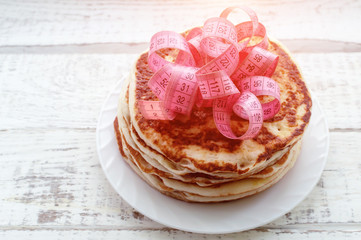 a stack of pancakes on a plate with a centimeter tape on top on a wooden table. the concept of an unhealthy lifestyle. overweight.