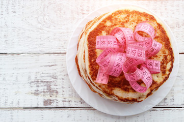 a stack of pancakes on a plate with a centimeter tape on top on a wooden table. the concept of an unhealthy lifestyle. overweight.