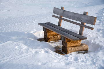 Wooden bench next to a winter hiking trail in the austrian alps in Lungau, Salzburg, Austria.