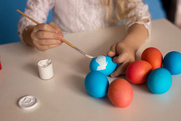 Obraz na płótnie Canvas preparation for the holiday of Easter: the child paints with white paint colored Easter eggs, a brush in children's hands.