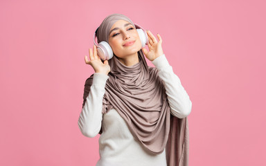 Joyful arabic girl in hijab listening favorite music with wireless headphones