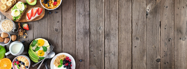 Healthy breakfast food banner with side border. Table scene with fruit, yogurt, smoothie bowl, nutritious toasts, cereal and egg skillet. Top view over a rustic wood background. Copy space.